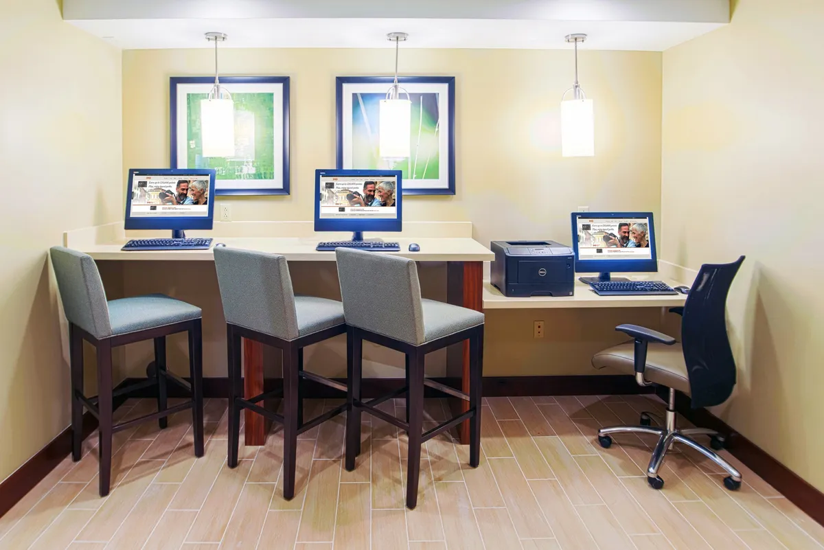 A modern business center outfitted with computer workstations, contemporary light fixtures, and framed artwork. The environment is designed for productivity and comfort, perfect for handling business tasks or connecting online.