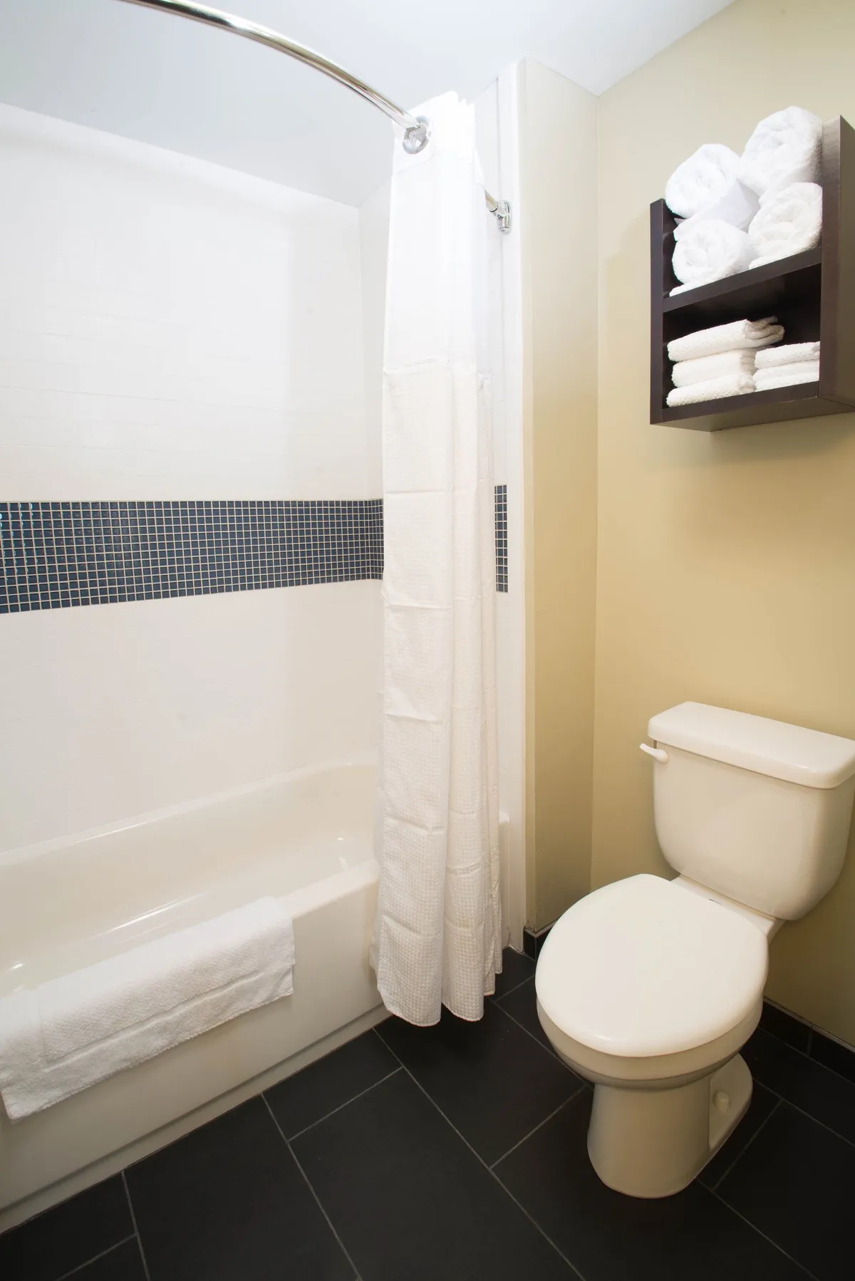 A modern, well-lit bathroom with a shower featuring a curtain, a toilet, and neatly folded towels on a rack. The spacious layout and accessible fixtures highlight inclusivity and ADA compliance.