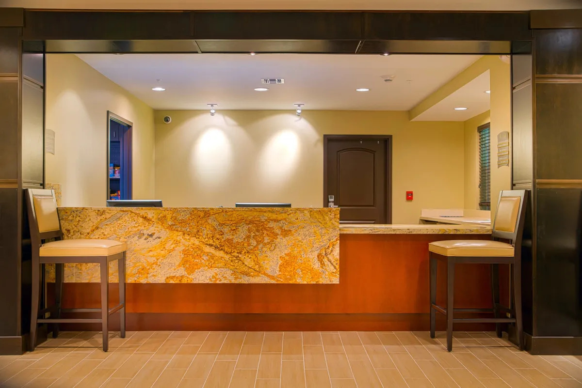 The image captures a welcoming hotel lobby with a granite reception desk, inviting stools, and warm-colored walls. This area serves as the first point of contact for guests, embodying the friendly, professional service the property offers.