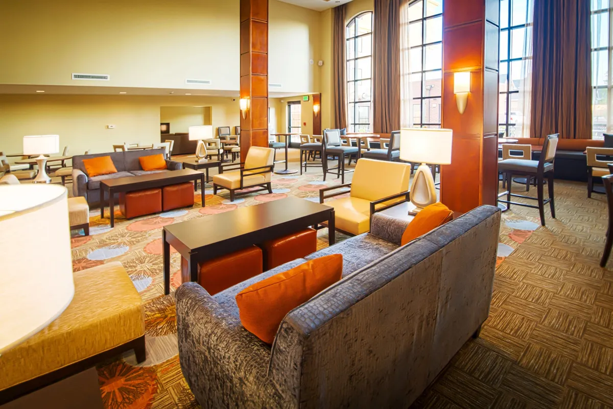 A bright, inviting living area with large windows, comfortable seating, decorative carpets, and stylish lamps—perfect for relaxing, socializing, or reading. The space conveys a sense of flexibility and homely comfort.